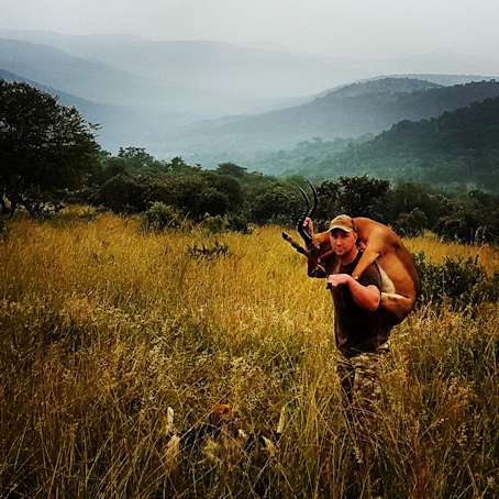 Hunter carrying blesbok trophy through golden KwaZulu-Natal grassland on South Africa hunting safari